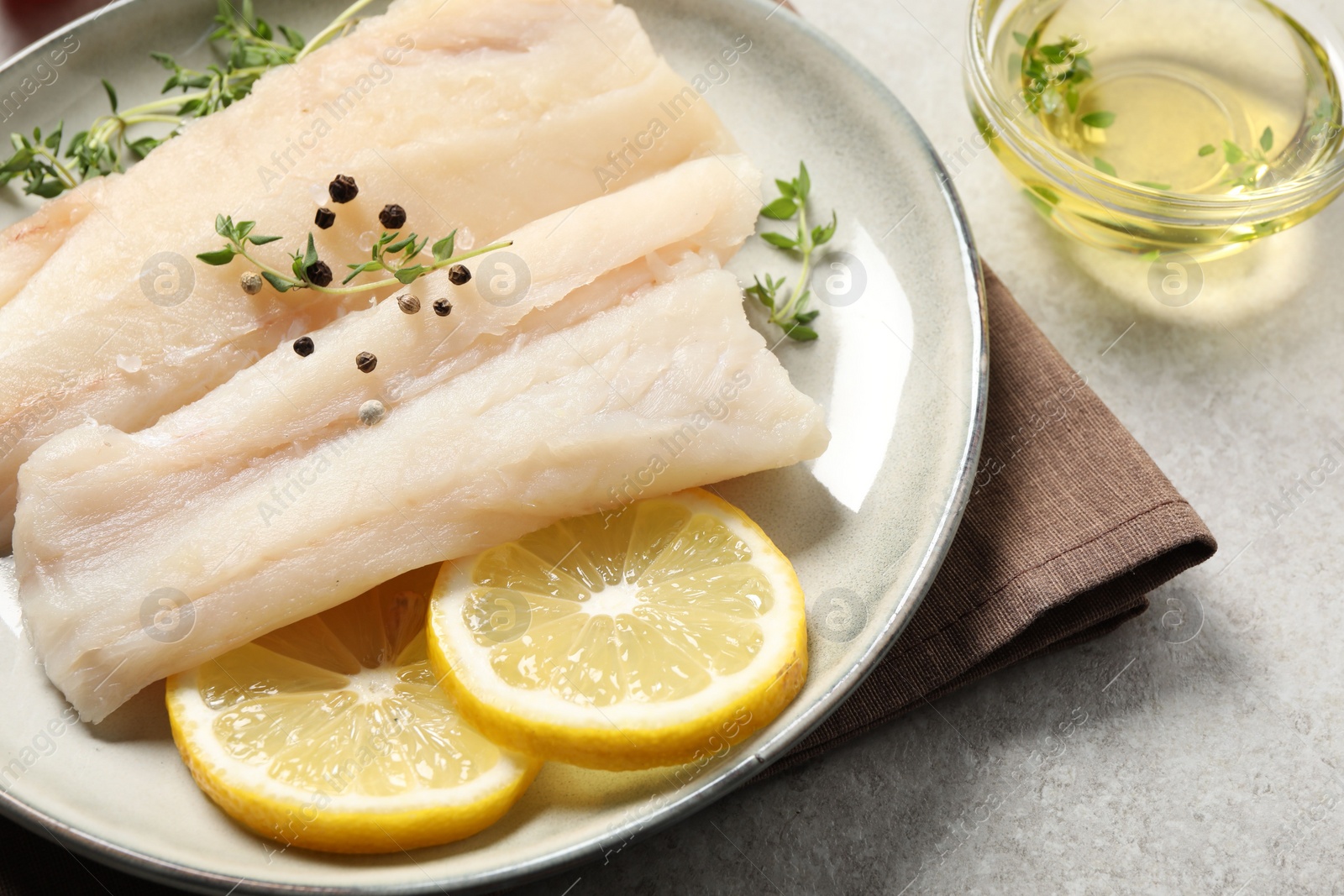 Photo of Plate with raw cod fish, spices, microgreens and lemon on grey table, closeup