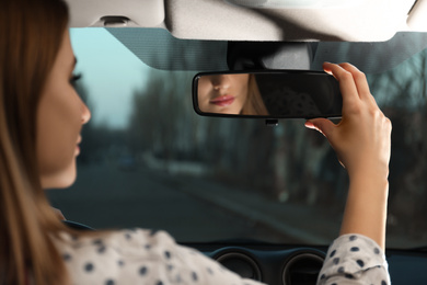 Photo of Young woman adjusting rear view mirror in car, closeup
