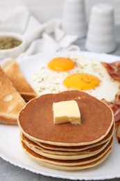 Tasty pancakes with fried eggs on grey table, closeup