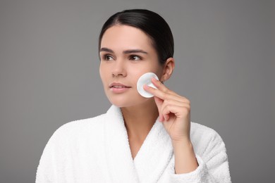 Photo of Young woman cleaning her face with cotton pad on grey background