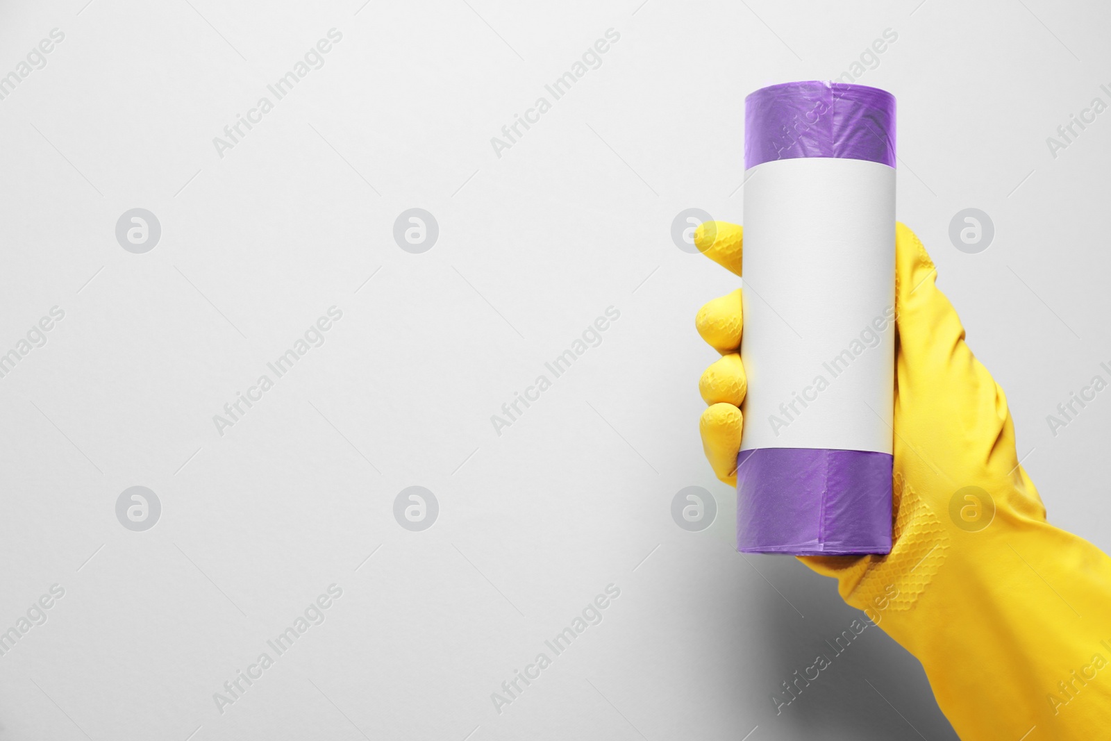 Photo of Janitor in rubber glove holding roll of violet garbage bags over light background, top view. Space for text