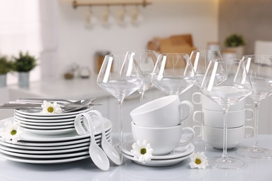 Photo of Set of clean dishware, glasses, cutlery and flowers on table in kitchen