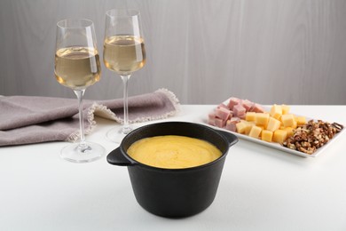 Photo of Fondue with tasty melted cheese, different products and aromatic wine in glasses on white table