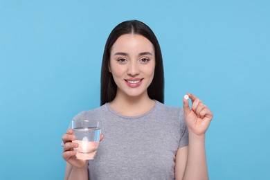 Photo of Beautiful young woman with glass of water and pill on light blue background