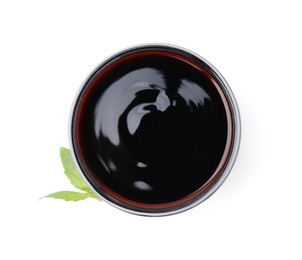 Glass bowl with balsamic glaze and basil leaves on white background, top view