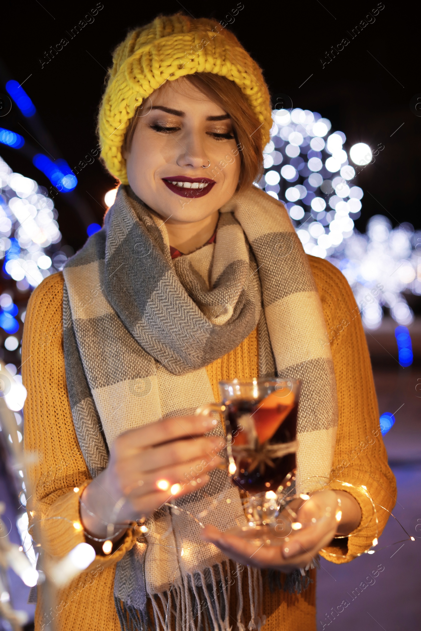 Photo of Woman with glass cup of mulled wine and garland at winter fair