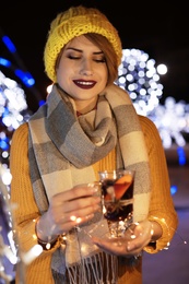 Woman with glass cup of mulled wine and garland at winter fair