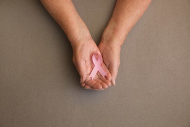Photo of Senior woman holding pink ribbon on grey background, top view. Breast cancer awareness