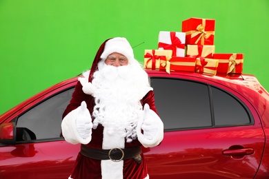 Authentic Santa Claus near car with presents on roof against green background