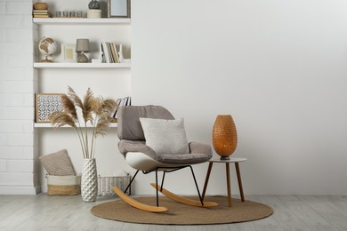 Photo of Soft rocking chair with pillow on rug near wall in room. Interior design