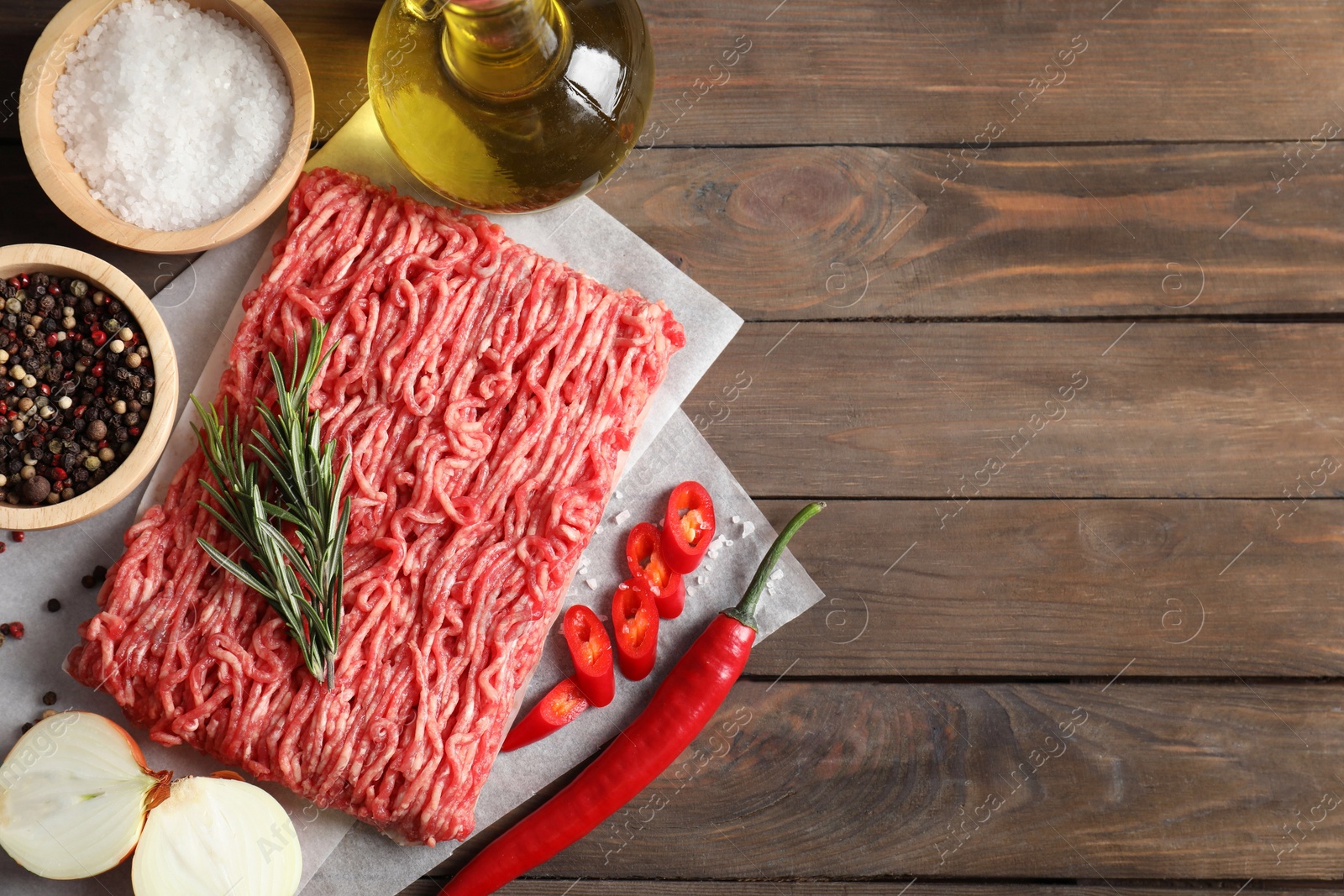 Photo of Raw ground meat, spices, rosemary, oil and onion on wooden table, flat lay. Space for text