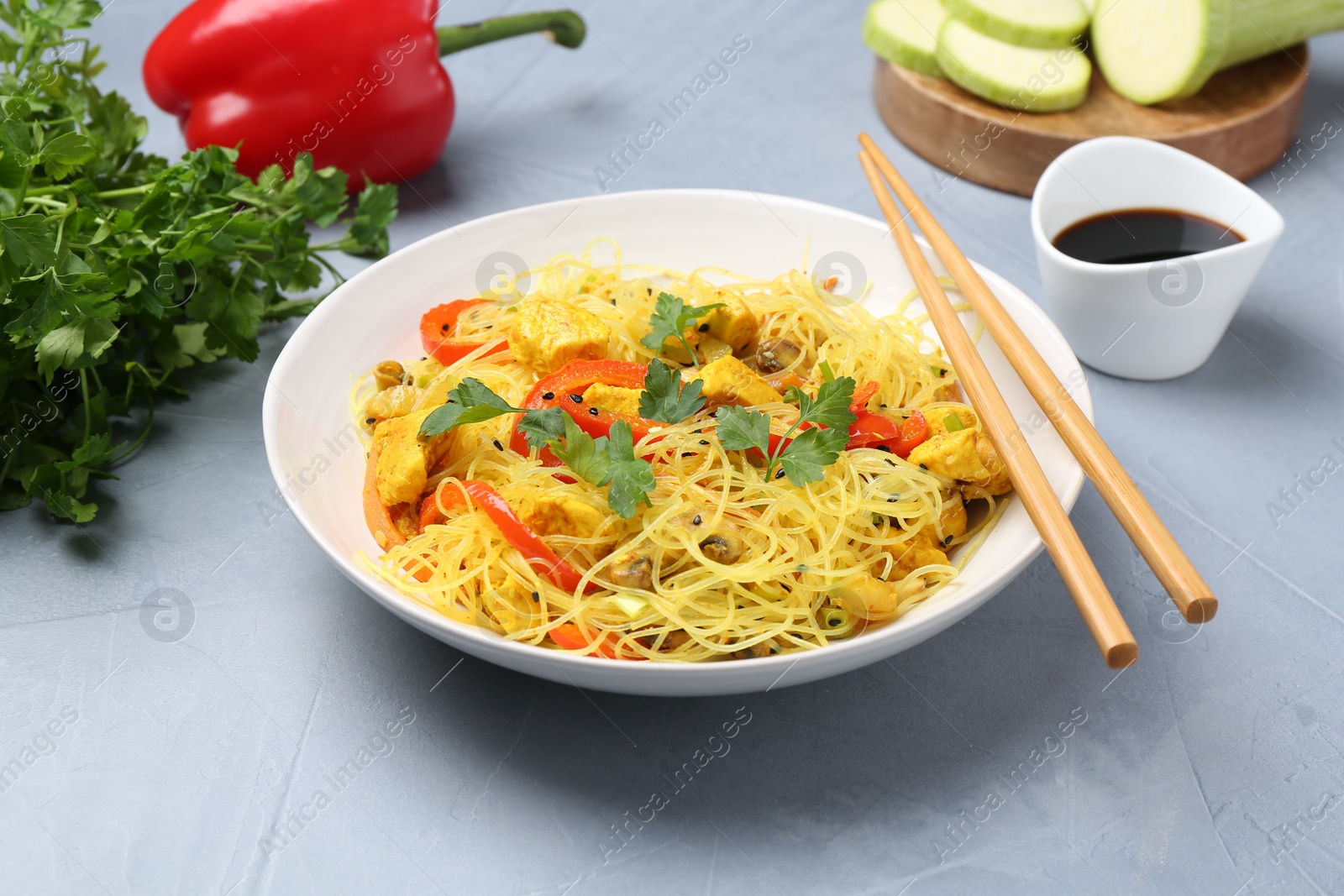 Photo of Stir-fry. Delicious cooked noodles with chicken and vegetables in bowl served on gray textured table