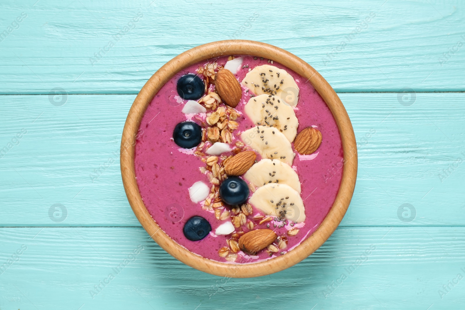 Photo of Delicious acai smoothie with granola and almonds in dessert bowl on light blue wooden table, top view