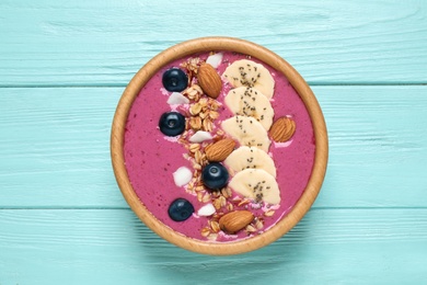 Photo of Delicious acai smoothie with granola and almonds in dessert bowl on light blue wooden table, top view