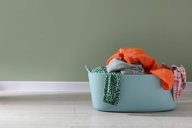 Laundry basket with clothes near light green wall indoors. Space for text