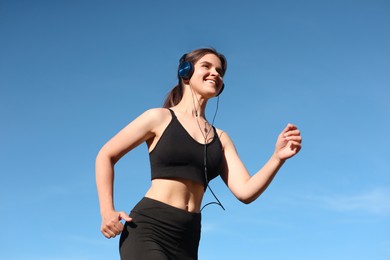 Photo of Young woman listening to music while running outdoors in morning, low angle view