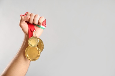Photo of Man holding golden medals on grey background, closeup. Space for design