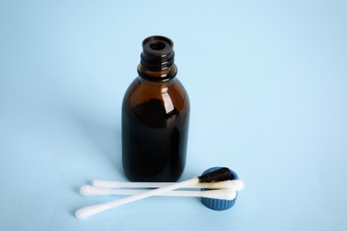 Photo of Bottle of medical iodine and cotton buds on light blue background