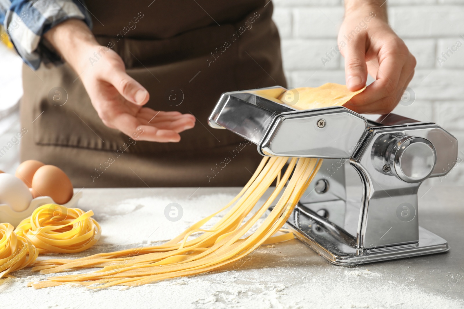 Photo of Young man preparing noodles with pasta maker at table