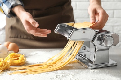 Young man preparing noodles with pasta maker at table