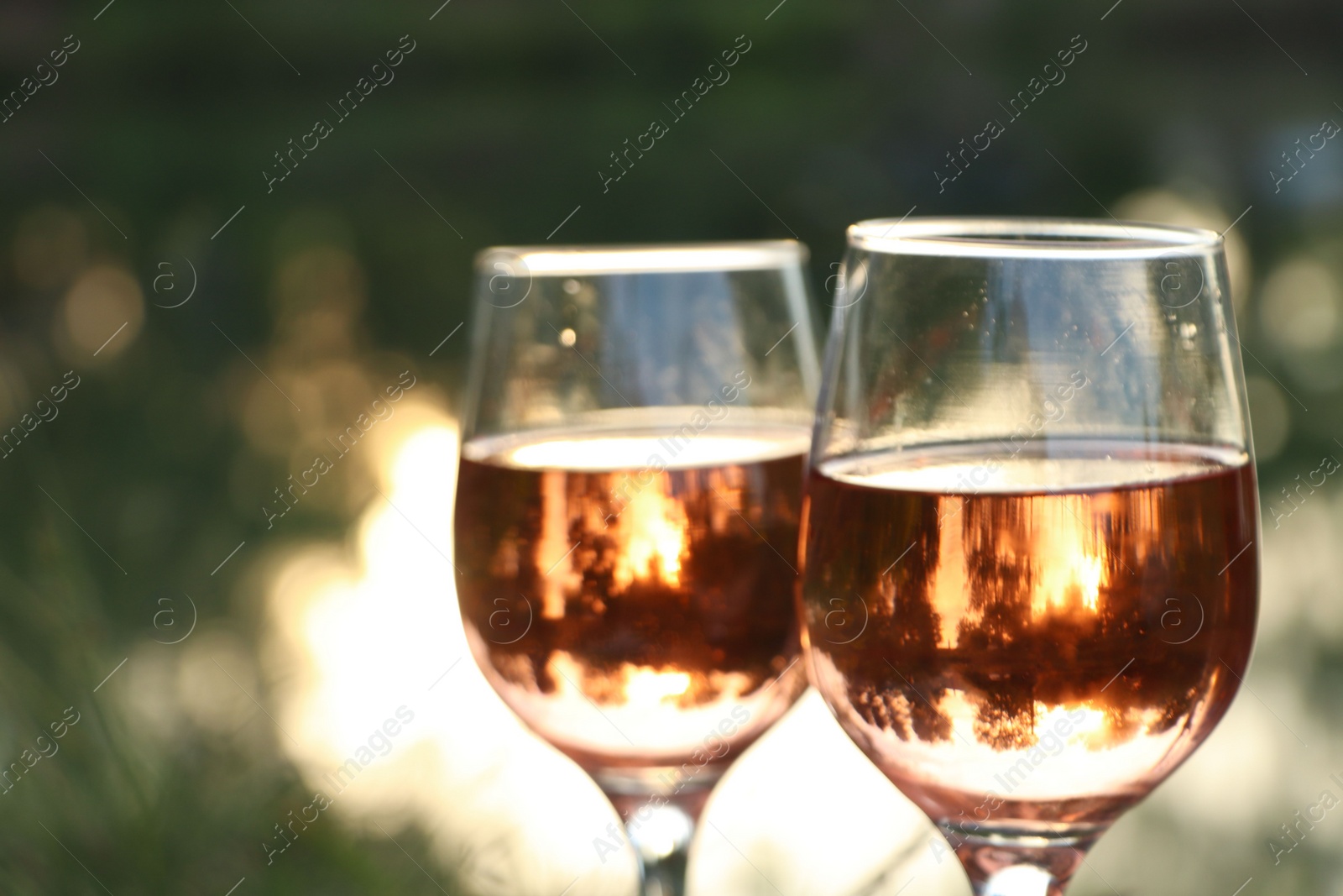 Photo of Glasses of tasty rose wine on blurred background, closeup and space for text. Picnic season