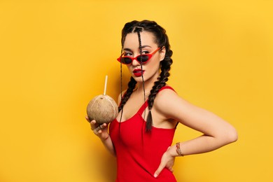 Young woman with fresh coconut on yellow background. Exotic fruit