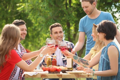 Photo of Young people with glasses of wine at table outdoors. Summer barbecue