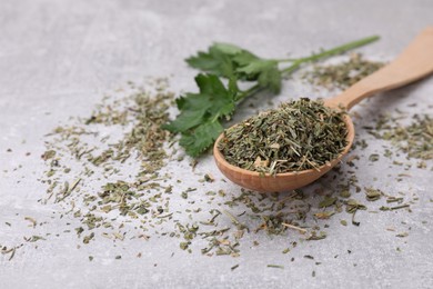 Photo of Wooden spoon with dried parsley and fresh leaves on light grey table, closeup. Space for text
