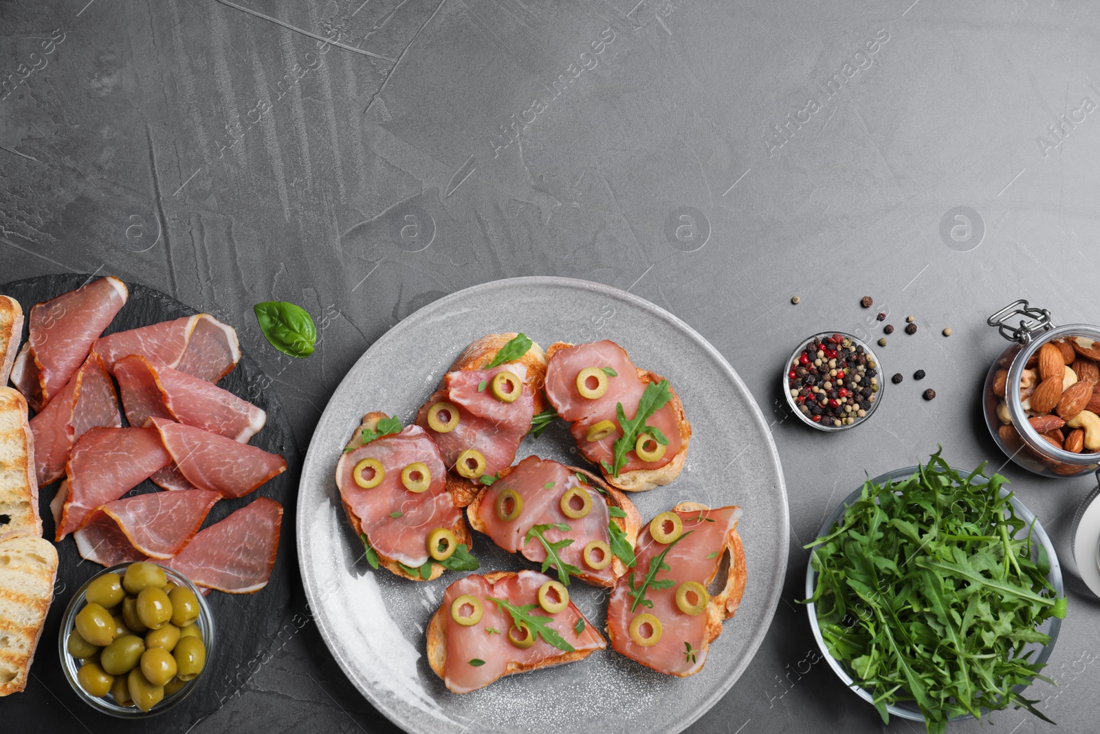 Photo of Delicious bruschettas with prosciutto and olives on grey table, flat lay. Space for text
