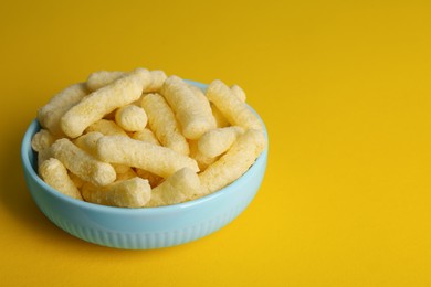 Bowl of corn sticks on yellow background, space for text