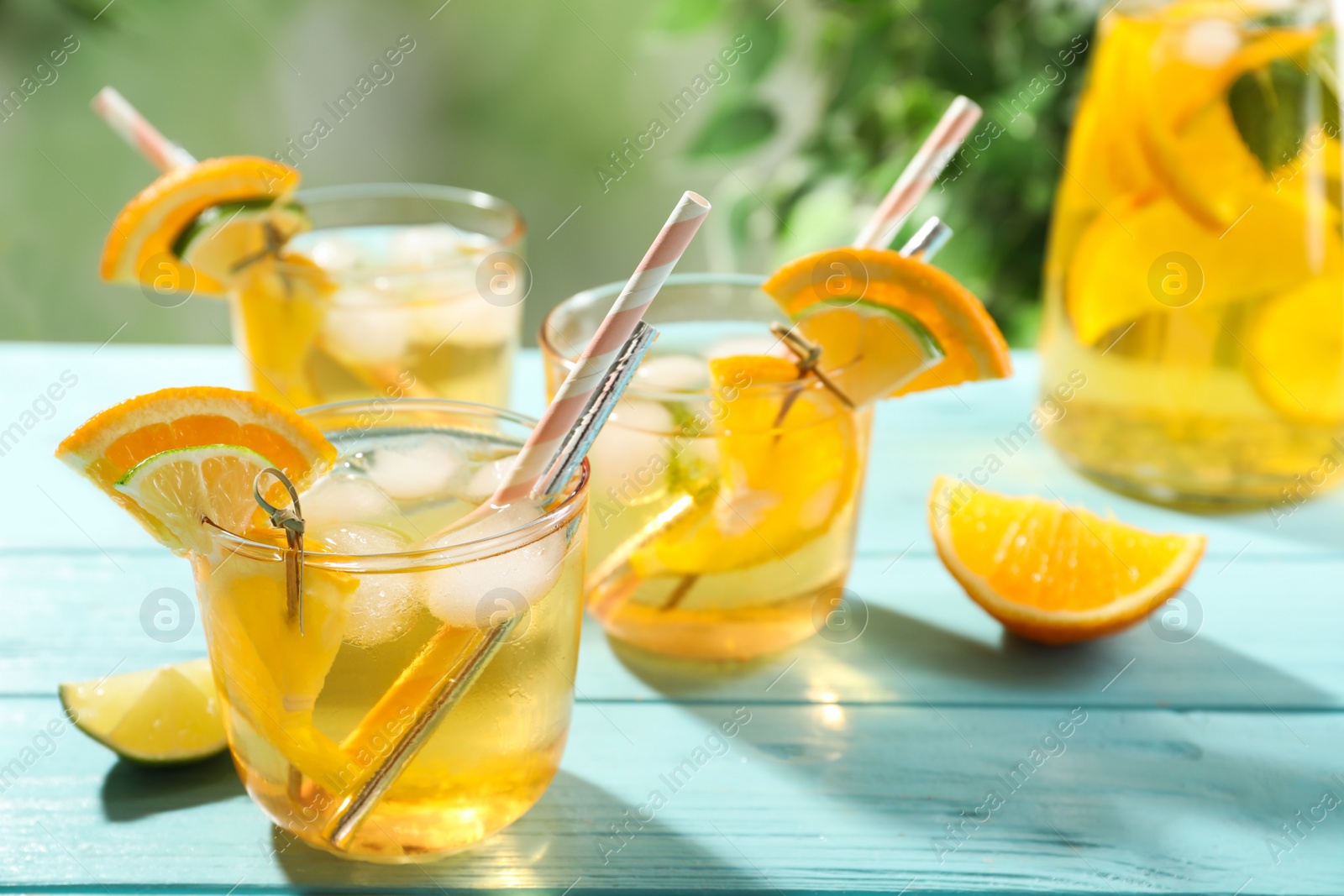 Photo of Delicious refreshing drink with orange and lime slices on light blue wooden table, closeup