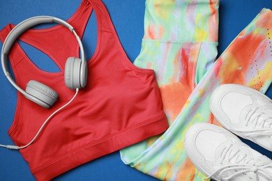 Photo of Stylish sportswear and headphones on blue background, flat lay