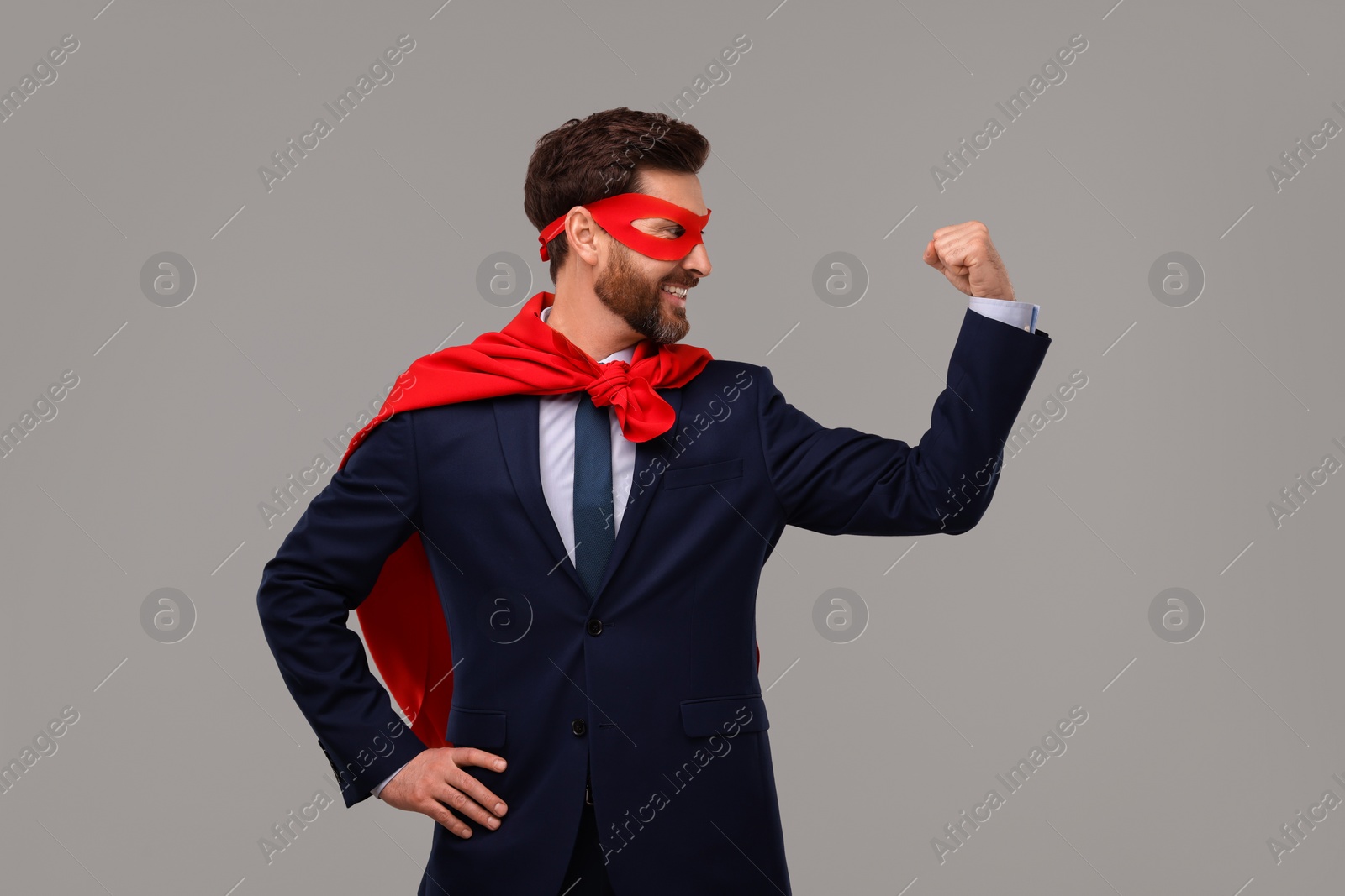 Photo of Happy businessman wearing red superhero cape and mask on beige background