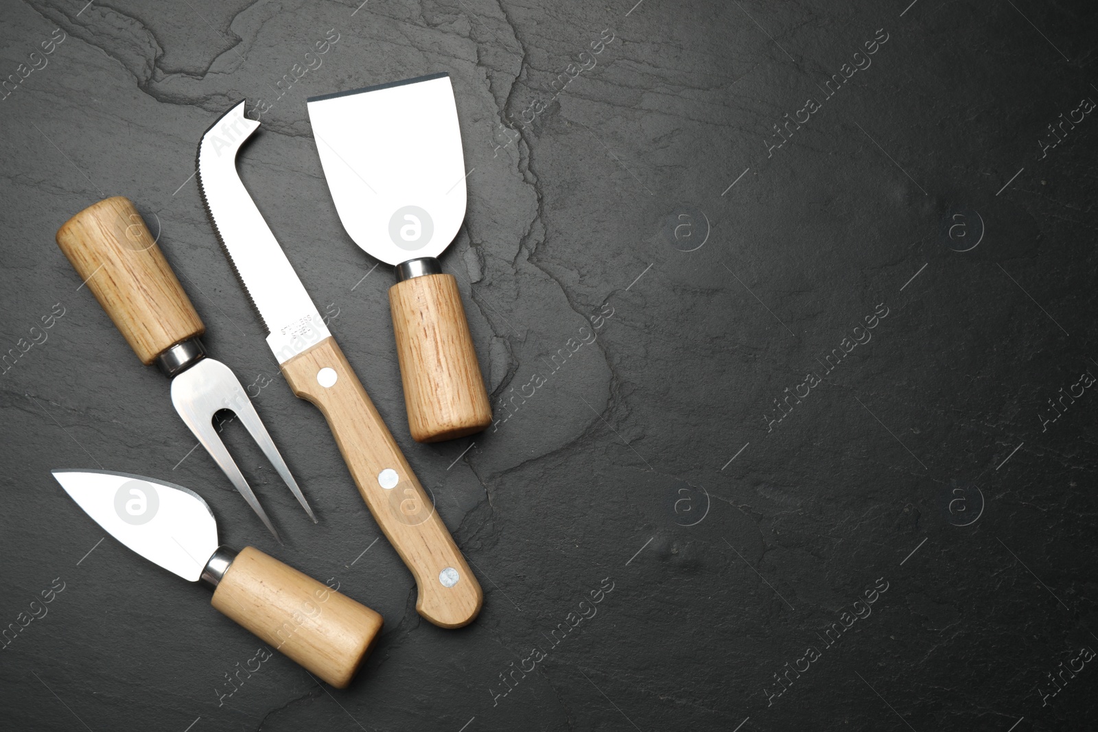 Photo of Cheese knives and fork on black stone table, flat lay. Space for text