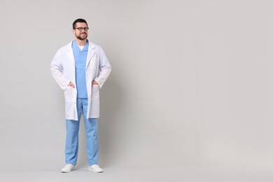 Full length portrait of smiling doctor on light grey background. Space for text