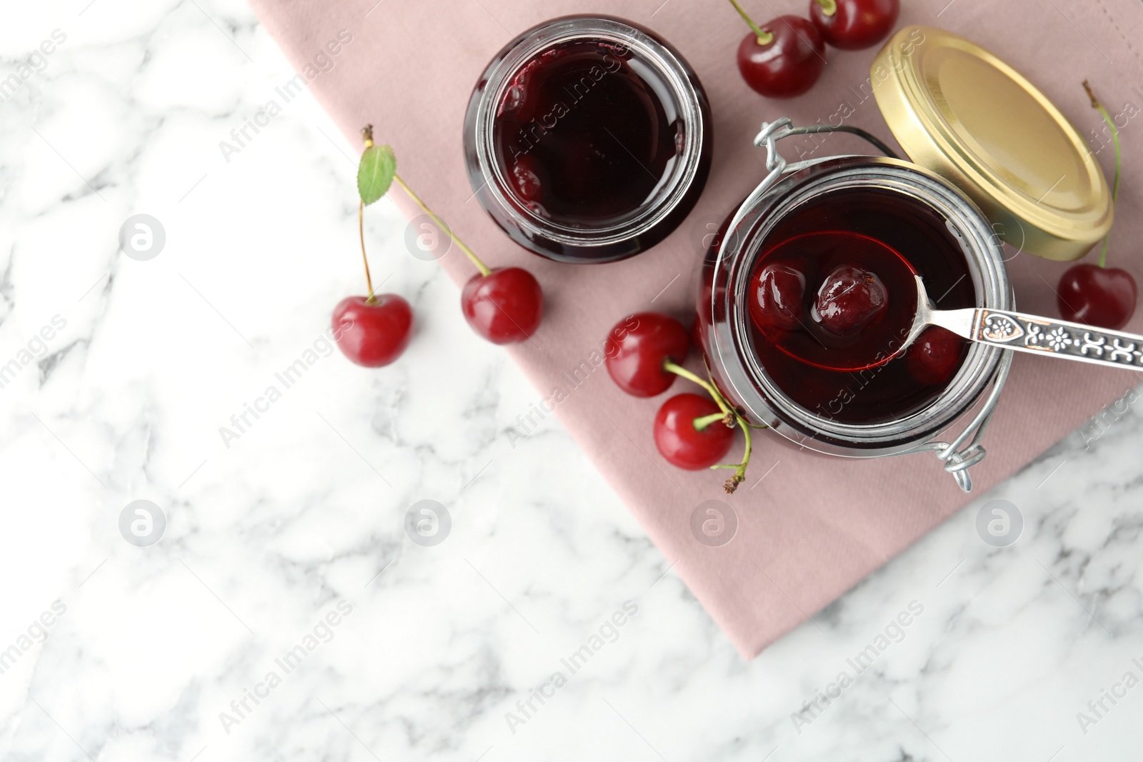 Photo of Jars of pickled cherries and fresh fruits on white marble table, flat lay. Space for text