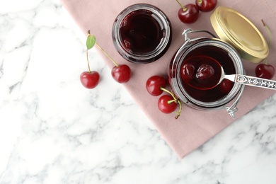 Jars of pickled cherries and fresh fruits on white marble table, flat lay. Space for text