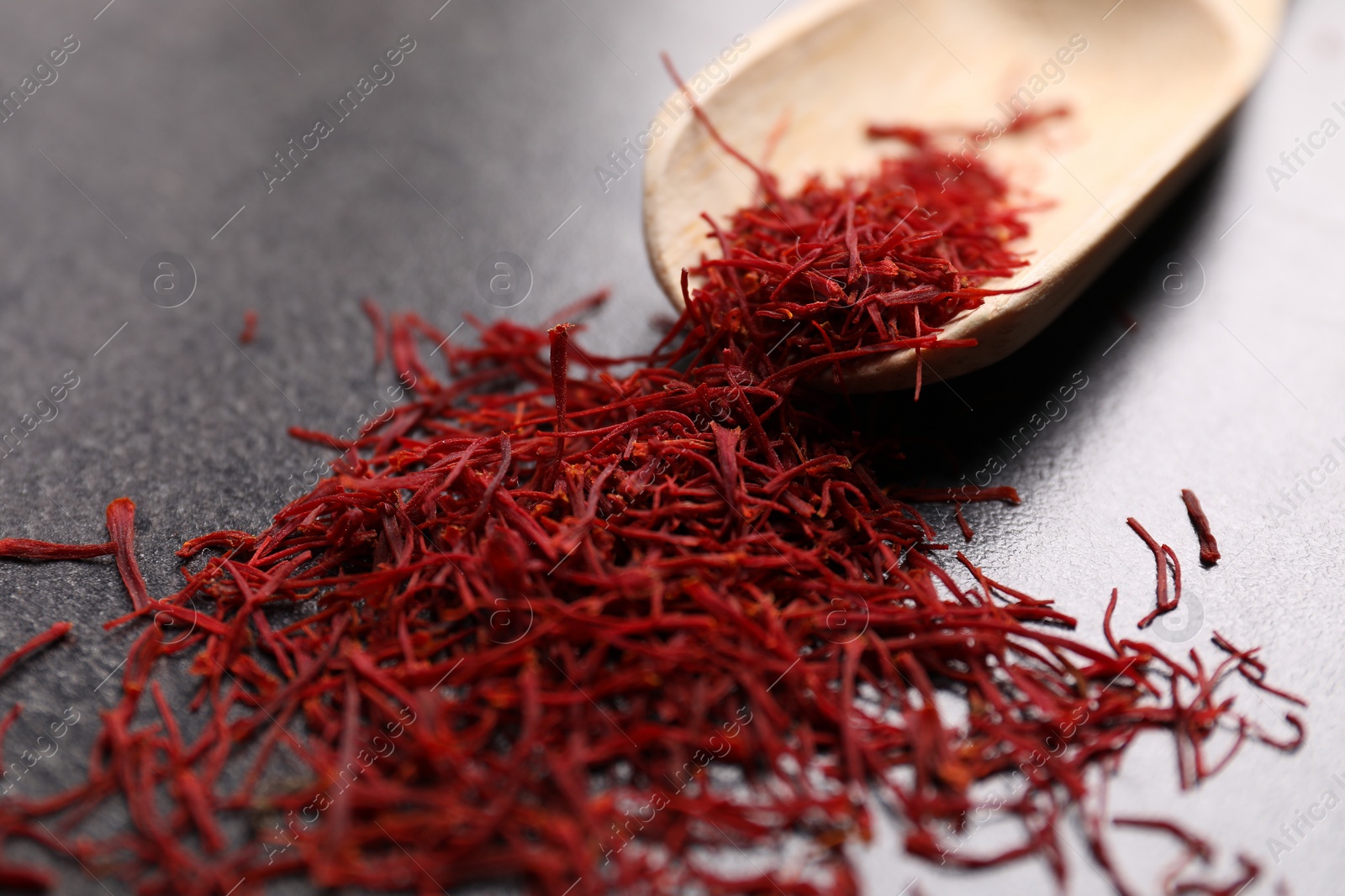 Photo of Aromatic saffron and wooden scoop on gray table, closeup