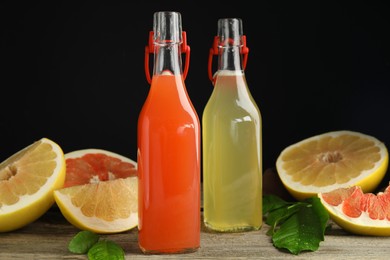 Glass bottles of different pomelo juices and fruits on wooden table against black background