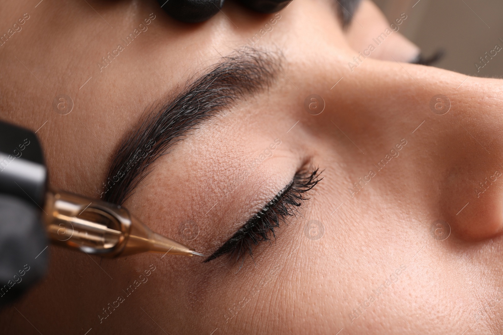 Photo of Young woman undergoing procedure of permanent eye makeup in tattoo salon, closeup