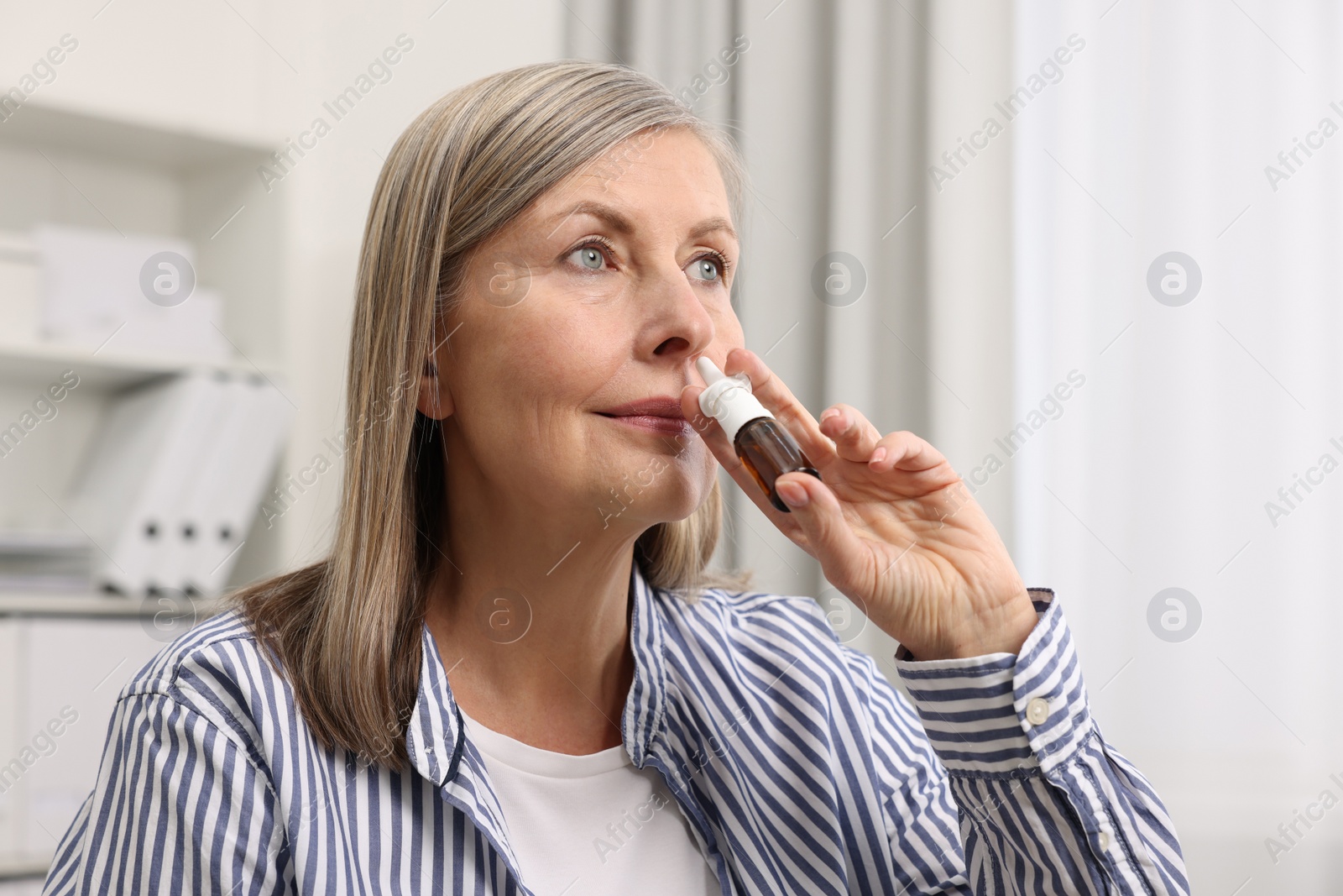 Photo of Medical drops. Woman using nasal spray indoors