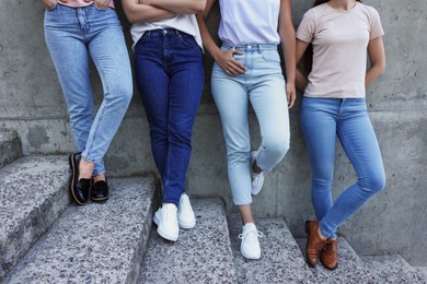 Photo of Women in stylish jeans on stairs near stone wall outdoors, closeup