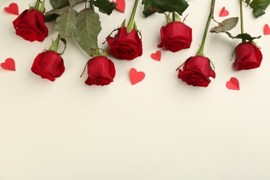 Photo of Beautiful red roses and paper hearts on light background, flat lay with space for text. Valentine's Day celebration