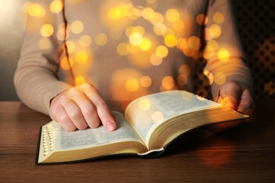 Image of Woman reading Bible at wooden table, closeup. Bokeh effect