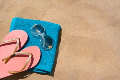 Photo of Folded soft blue beach towel with flip flops and sunglasses on sand, flat lay. Space for text