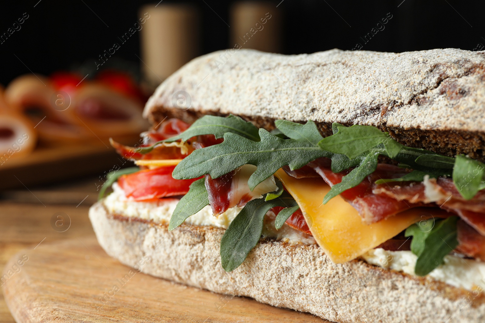 Photo of Delicious sandwich with fresh vegetables and prosciutto on wooden table, closeup