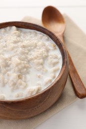 Photo of Tasty boiled oatmeal in bowl and spoon on white table, closeup