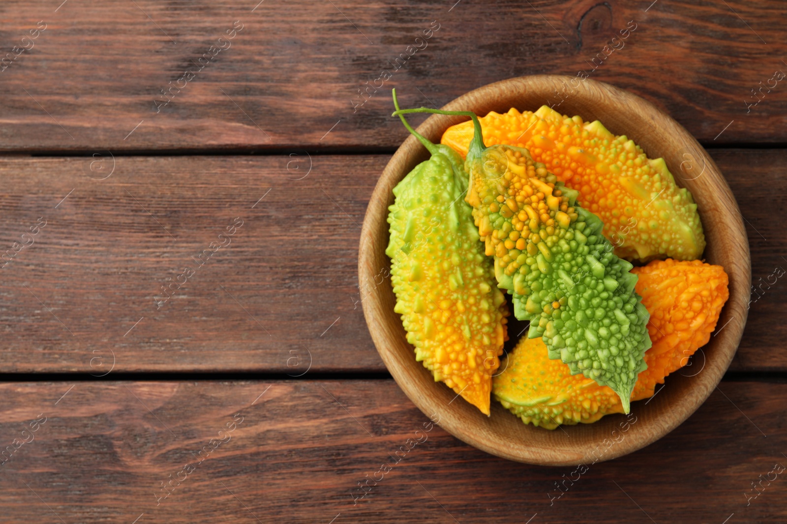 Photo of Bowl with fresh bitter melons on wooden table, top view. Space for text