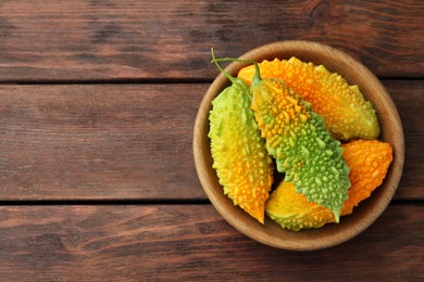 Photo of Bowl with fresh bitter melons on wooden table, top view. Space for text