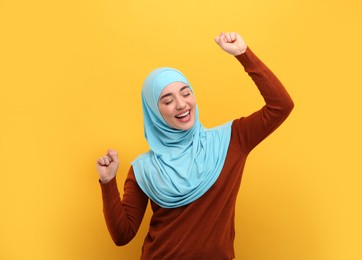 Photo of Muslim woman in hijab dancing on orange background